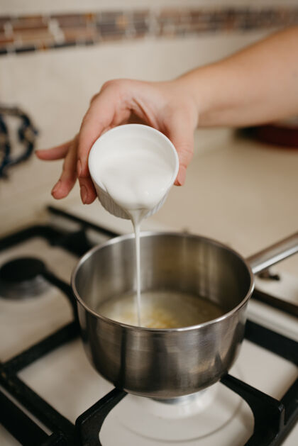 特写一张照片 一个女人的手从杯子里往平底锅里倒奶油 在煤气炉上放柠檬汁和香料手自制配料