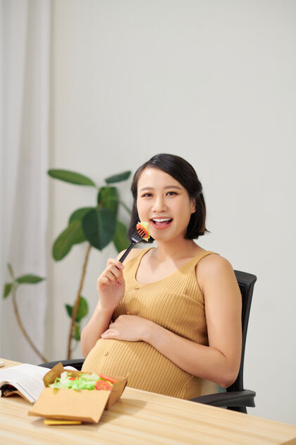 孕妇一位年轻的孕妇站在家庭办公室里使用平板电脑午餐美丽沙拉