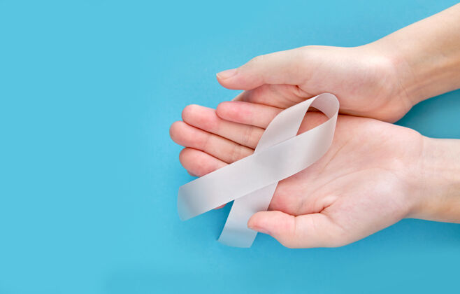 癌症白色表面上女人手上的银色象征丝带人哮喘磁带
