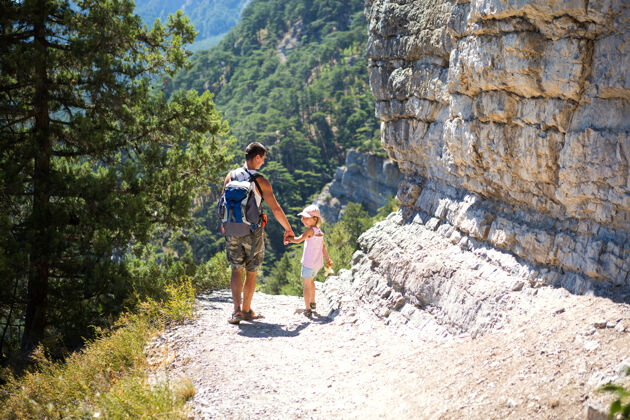 背包爸爸和女儿去山间小径徒步旅行积极的家庭假期活跃新鲜空气石墙