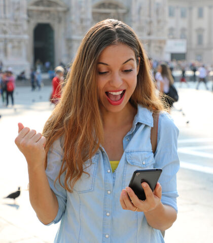 手机女人在外面的大街上用智能手机在线接收好消息兴奋观看庆祝