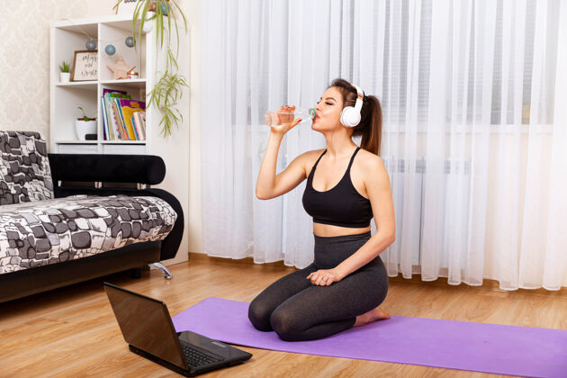 健身房爱运动的女人喝水 坐在健身垫上客厅上课健康的生活方式