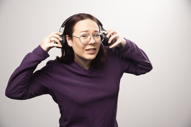 肖像戴着眼镜的年轻女子戴着耳机在听音乐 这是一张高质量的白色照片年轻眼镜站立