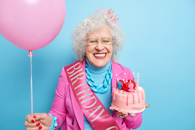 乐趣开心的老太太横拍笑容可掬有呵护的样子庆祝102岁生日快乐的陪伴看着美丽的晚年捧着甜蛋糕和充气的氦气球姿势室内享受