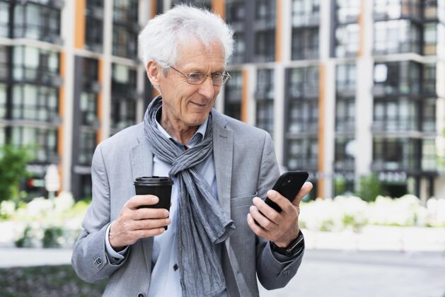 城市城里时髦的老人一边喝咖啡一边用智能手机城市移动设备