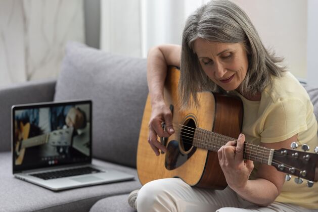 家庭资深女士在家沙发上用笔记本电脑上吉他课女人原声吉他成人
