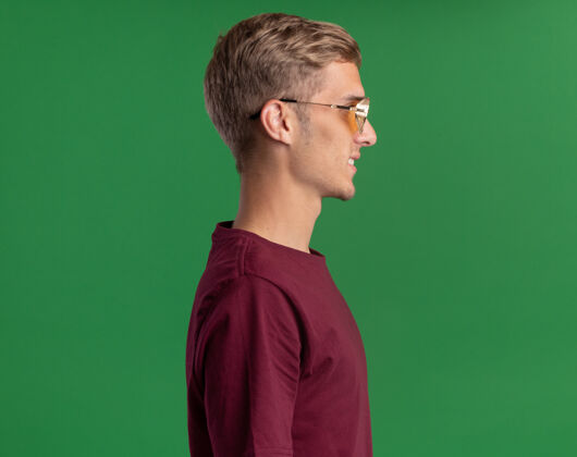 人微笑着站在侧视图年轻帅哥穿着红色衬衫和眼镜隔离在绿色墙壁与复制空间人微笑男人