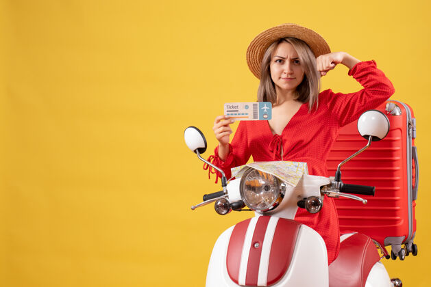 冒险正面图：身穿红色连衣裙的年轻女士手持车票 在轻便摩托车上展示手臂肌肉持有手提箱女人