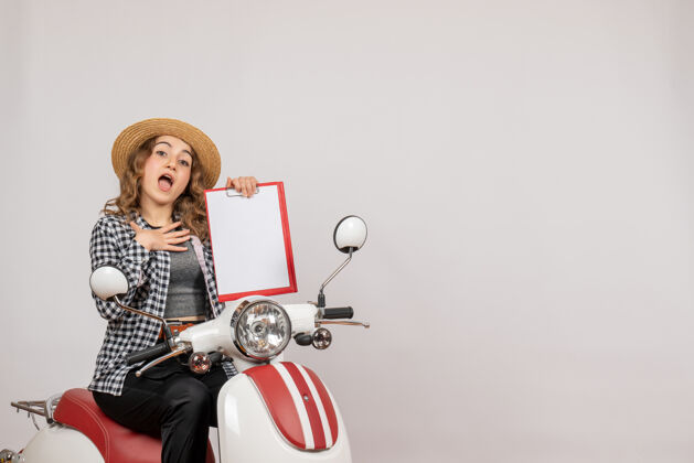 人前视图：坐在轻便摩托车上拿着红色剪贴板的年轻女子人红色摩托车