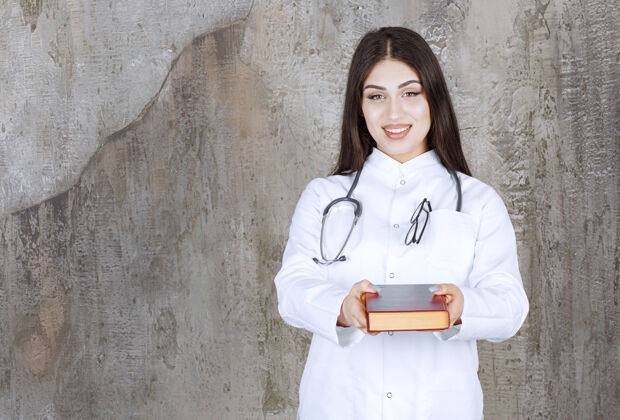 疾病微笑的年轻女医生在灰墙上献书工作医生制服