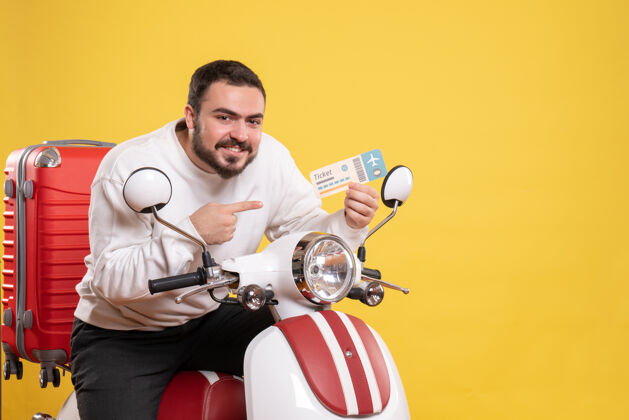 黄色正面图是一个年轻的微笑着的旅行男子坐在摩托车上 手提箱上拿着票 背景是孤立的黄色车票微笑成人