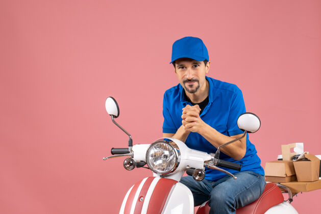 背景前视图微笑的信使家伙戴着帽子坐在粉彩桃背景踏板车棒球摩托车人物