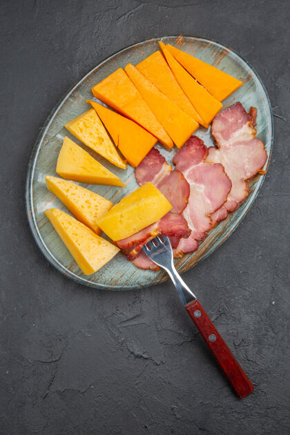 抹刀美味的香肠和奶酪片放在蓝色的盘子里 背景是深色的厨房用具饭菜头顶