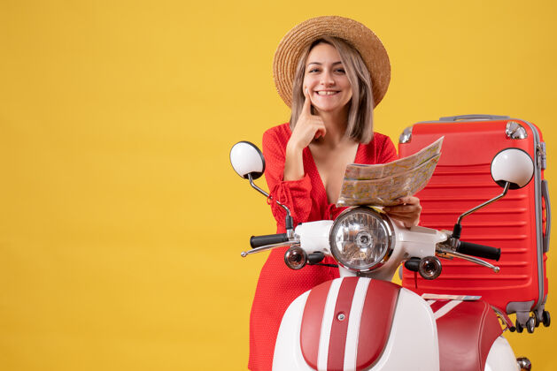 车辆微笑着的穿着红裙子的年轻女士拿着地图靠近轻便摩托车摩托车肖像衣服