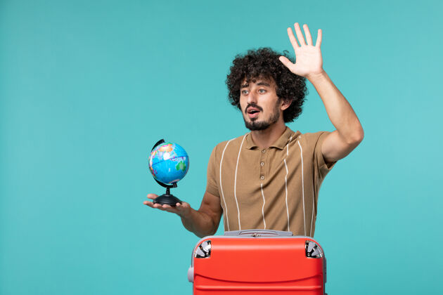 风景度假的男人手里拿着一个小地球仪 红色的袋子在蓝色的上面挥舞蓝色地球航行