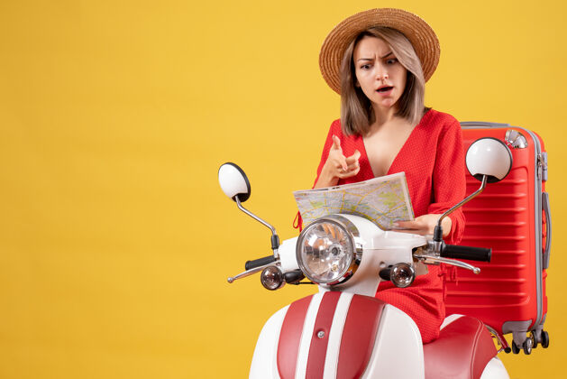 人戴着巴拿马帽的漂亮女孩骑着轻便摩托车 提着红色手提箱 看着地图肖像坐着手提箱