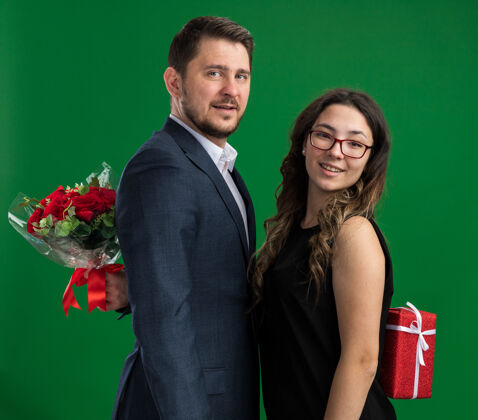 年轻年轻漂亮的夫妇幸福的男人和女人藏礼物从对方幸福的爱在一起庆祝情人节站在绿色的墙男人礼物女人