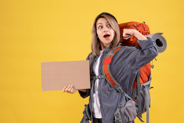 可爱一个背着红色背包的女旅行者 手里拿着展示手臂肌肉的纸板背包女士时尚