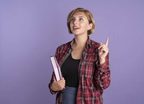 女孩惊讶的年轻斯拉夫学生女孩指着手中的书和笔记本学生紫色向上