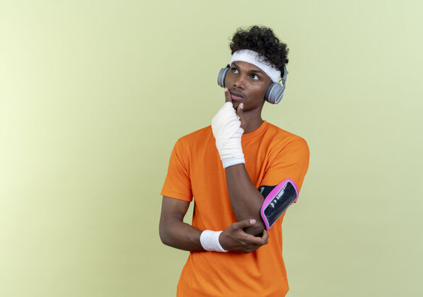 男人看着一边思考的年轻的美国黑人运动男子戴着头带和腕带和电话臂带耳机把手放在下巴上年轻壁板下巴