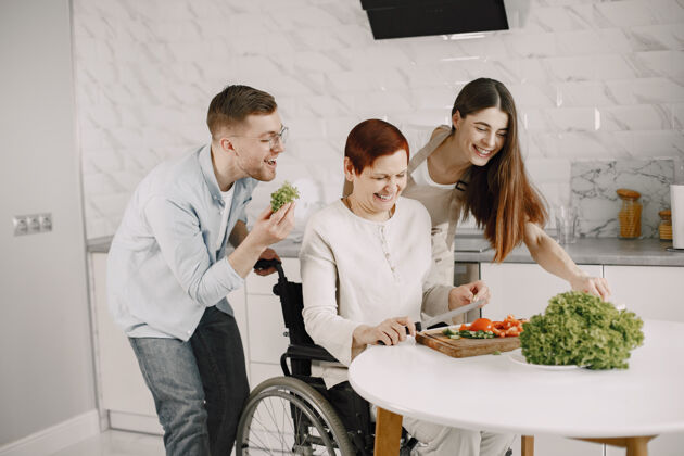 家庭轮椅上的老太太在厨房做饭残疾人夫妇在帮她膳食房间房子