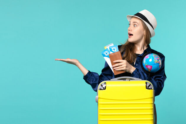 航行前视图年轻女子拿着机票和地球仪在淡蓝色背景的飞机海上度假旅行旅程微笑成人