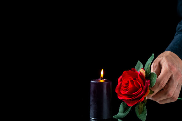 葬礼黑色蜡烛的正面图 红色玫瑰和黑色表面上的男性手红燃烧风景
