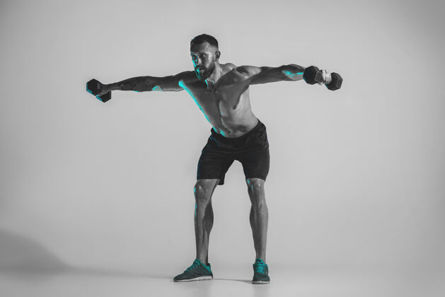 肌肉蓝色月光年轻的白种人健美运动员在霓虹灯下的工作室背景下训练肌肉发达的男模体重运动 健美 健康的生活方式 运动和行动的概念人无袖运动员