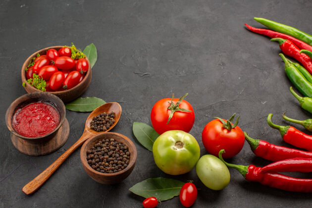 碗底视图一碗樱桃西红柿 红 绿辣椒和西红柿 一碗番茄酱和黑胡椒 一把勺子放在黑桌子上叶子食物胡椒