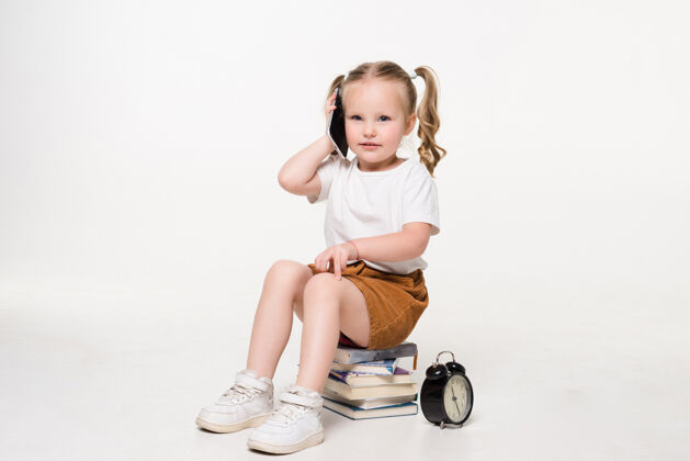 学校一个小女孩坐在一堆书上讲电话的画像休闲女孩小女孩