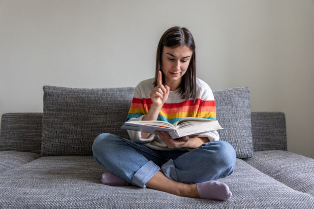 文学一个穿着鲜艳毛衣的女孩在家的沙发上看书房子华丽学生