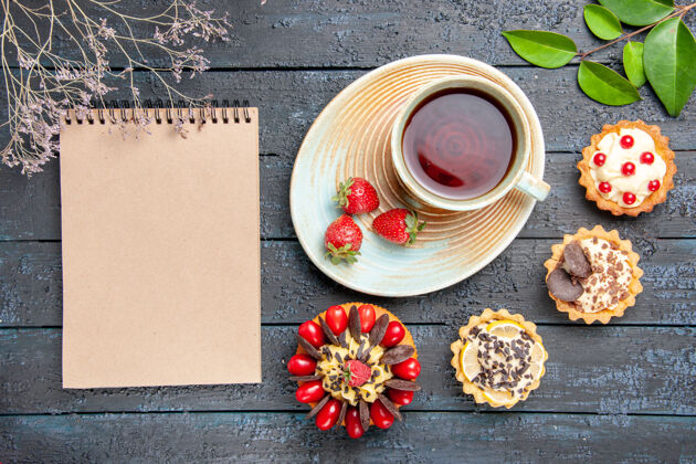 食物顶视图一杯茶和草莓放在茶碟上干橙子馅饼叶子浆果蛋糕和一本笔记本放在深色的木桌上托盘美食盘子