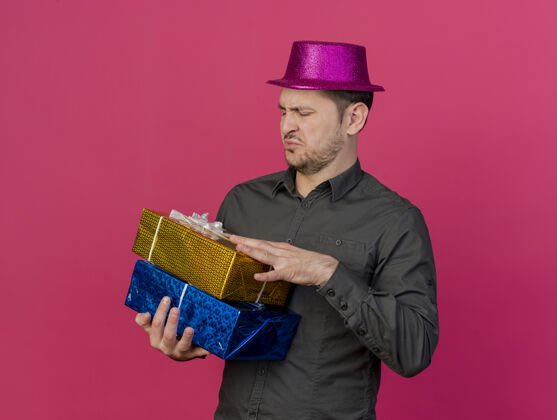 礼物一个戴着粉红色帽子的年轻人拿着礼物盒 看着孤立的粉红色盒子戴着粉色年轻人