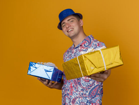 帽子带着微笑的年轻人戴着蓝色的帽子拿着礼物盒孤立在橙色派对戴着蓝色