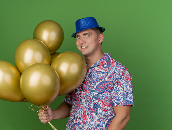 戴着快乐的年轻人戴着蓝帽子拿着气球孤立在绿色的聚会帽子派对抱着