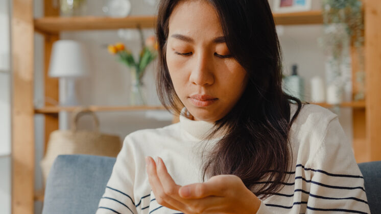 距离生病的亚洲年轻女子拿着药丸坐在家里的沙发上吃药药房咳嗽药物