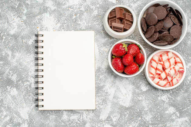 水果顶视图碗草莓糖果和巧克力和一个笔记本在灰白色的地面上浆果多汁成熟