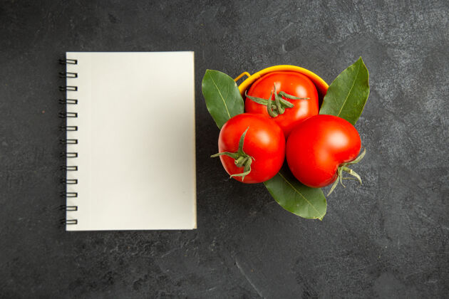 新鲜顶视图一桶西红柿和月桂叶和一个笔记本在黑暗的地面上深色木本植物水果