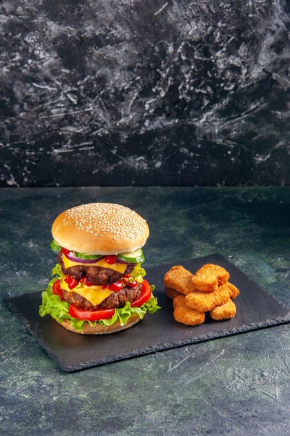 餐厅美味的肉三明治的垂直视图 深色托盘上有绿色的西红柿和黑色表面上的鸡块正餐托盘美味
