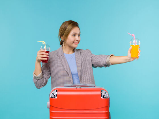 蓝色正面图：度假中的女性拿着新鲜饮料在蓝色背景上进行海上旅行度假飞机旅行旅行肖像举行假期