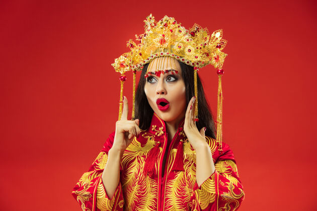 指向中国传统的优雅女子在摄影棚的红色背景美丽的女孩穿着民族服装中国新年 优雅 优雅 表演者 表演 舞蹈 女演员 服装的概念服装穿着传统