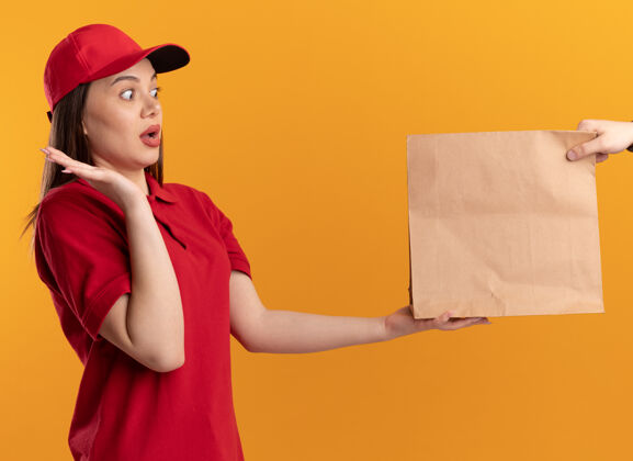 送货一个穿着制服的焦急漂亮的女送货员举起手 把纸包递给一个穿橙色衣服的人焦虑站有人