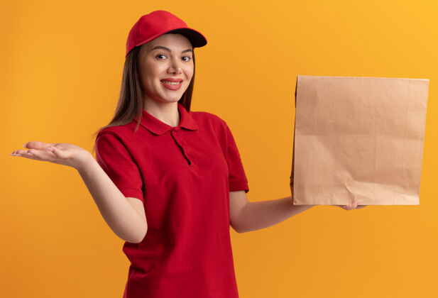 橘子穿着制服的漂亮送货员高兴地把手张开 手里拿着橘黄色的纸包送货打开包装