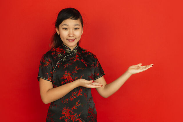 旗袍做手势 邀请客人2020年中国新年快乐红色背景上的亚洲少女肖像穿着传统服装的女模特看起来很快乐庆祝 人类情感复制空间服饰服装女性