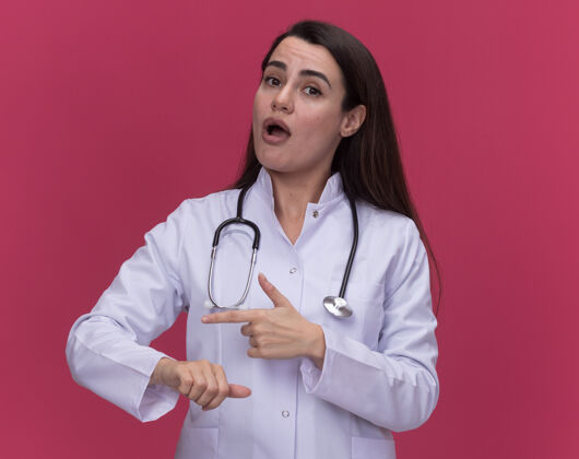 听诊器令人印象深刻的年轻女医生穿着医用长袍听诊器点在粉红色的两侧点女医疗