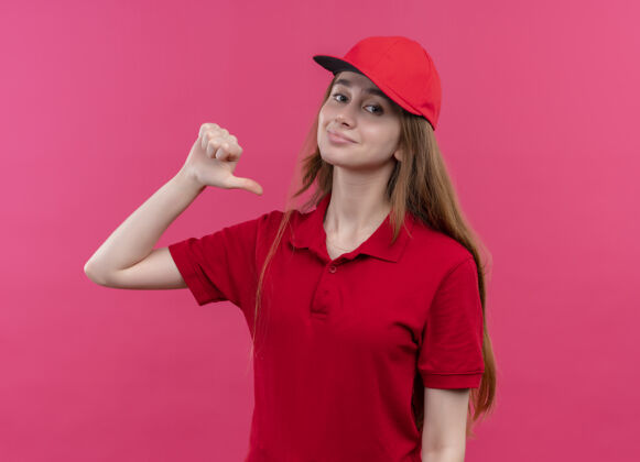 交货一个穿着红色制服的自信的年轻送货女孩在孤立的粉色空间里指着自己指向粉色制服