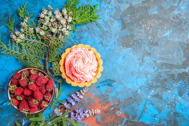 玫瑰蓝色表面上带有覆盆子的粉红色面团奶油碗的小馅饼俯视图质地糕点礼物