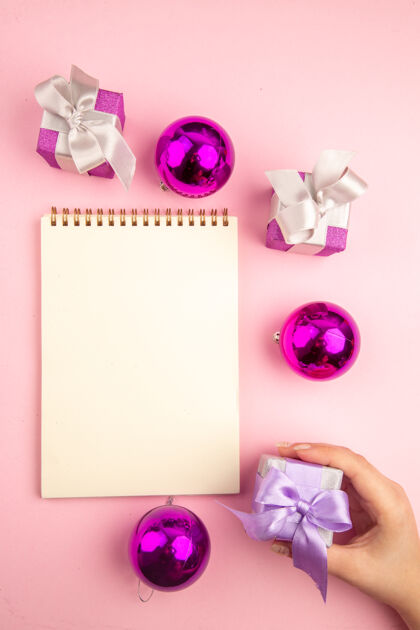 圣诞节顶视图的小礼物圣诞树玩具和记事本上的粉红色表面记事本礼物树