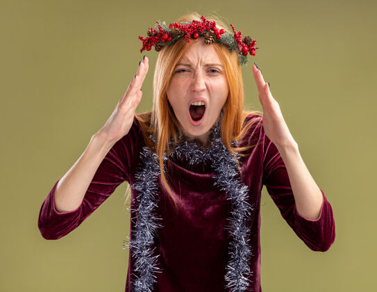 脖子愤怒的年轻漂亮的女孩穿着红裙子 脖子上戴着花环和花环 背景是橄榄绿花环愤怒圣诞快乐