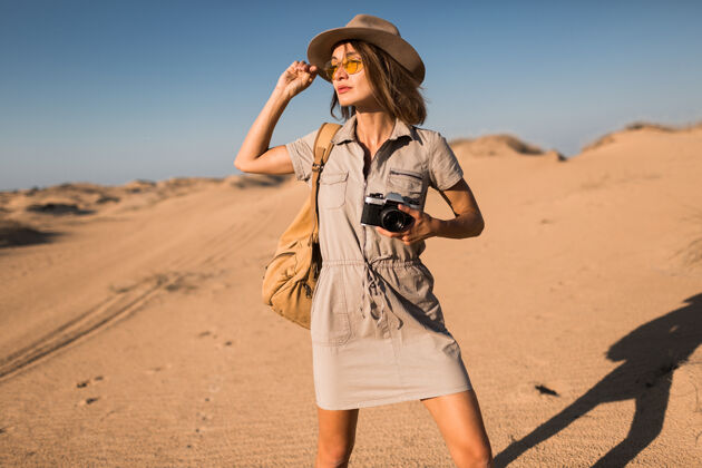 女人穿着卡其色衣服的时髦年轻女子在沙漠中行走 在非洲旅行 戴着帽子和背包 用老式相机拍照狩猎旅游美丽